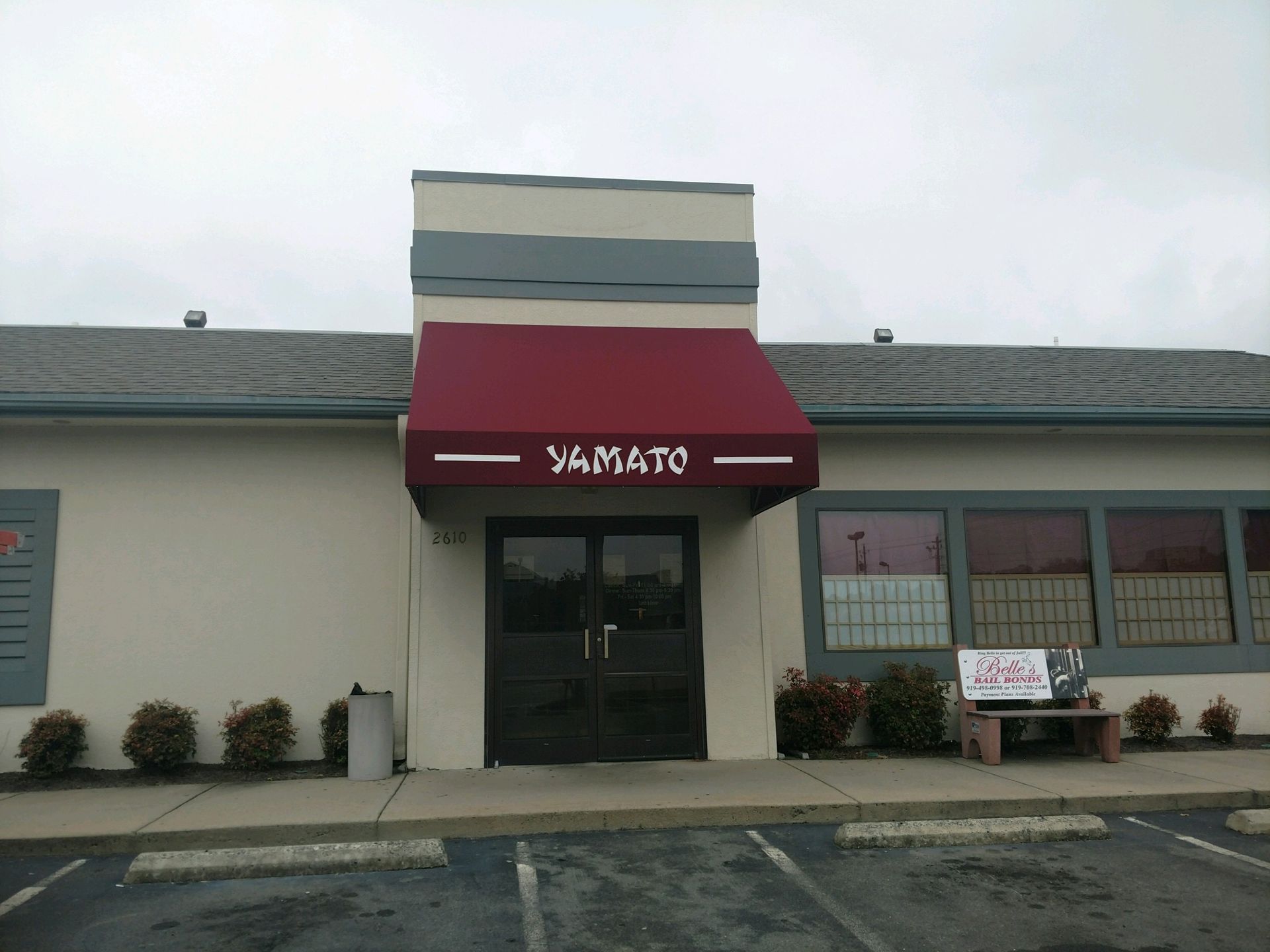 Storefront with a red awning and glass entrance in a strip mall parking lot