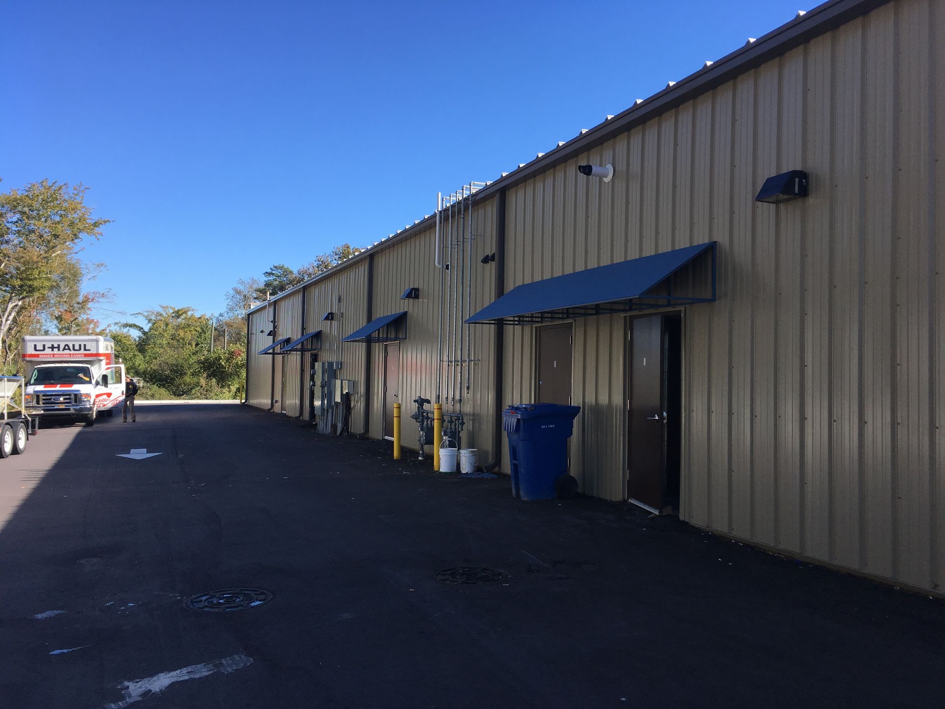 Long beige building with blue awnings along an empty parking lot, with a truck at the far end.