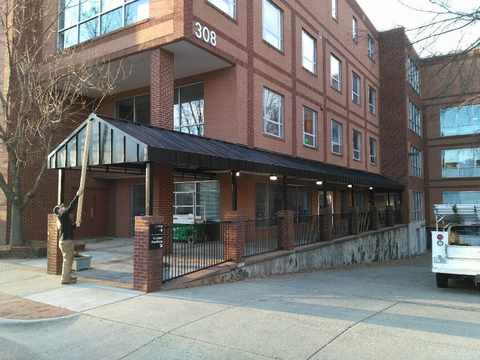 Brick building entrance with black awning, sidewalk ramp, and glass doors at a street corner.