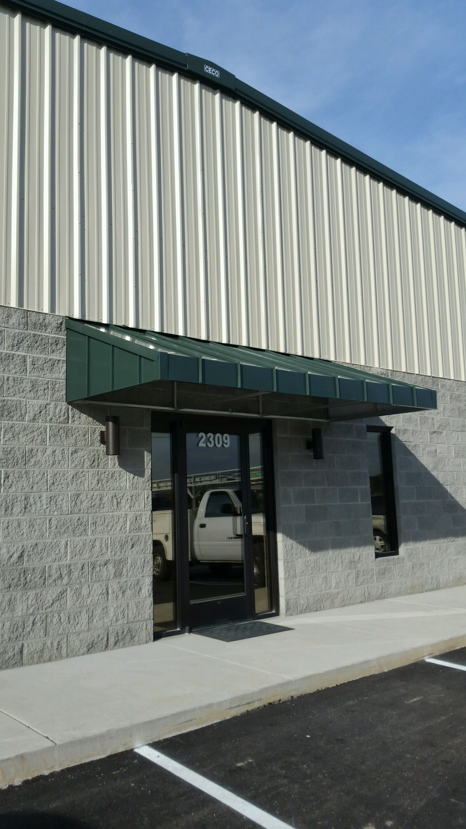 Building entrance with gray brick walls, striped siding, and a green awning over a glass door.