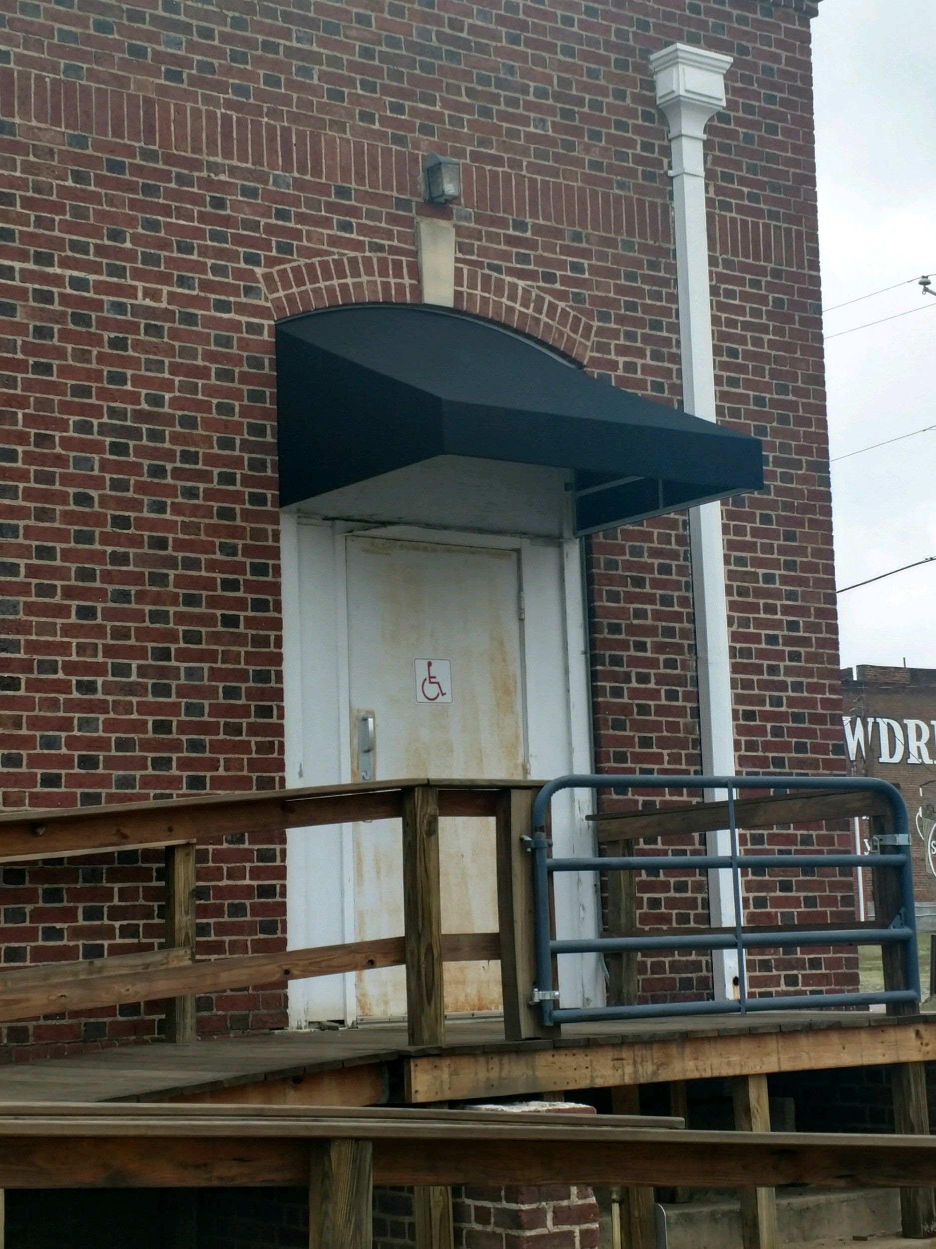Brick building exterior with white door, black awning, and wooden deck railing.
