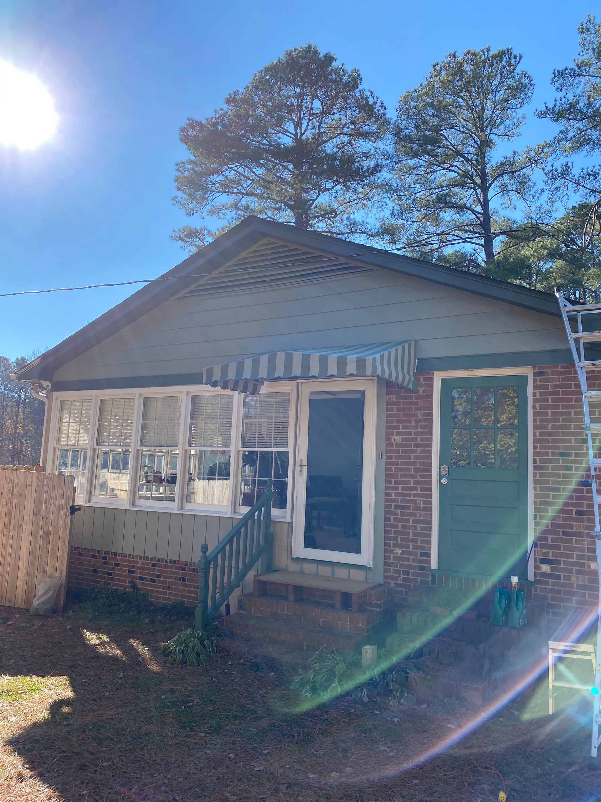 Small house with a screened porch and blue door in bright sunlight, viewed from the front yard.