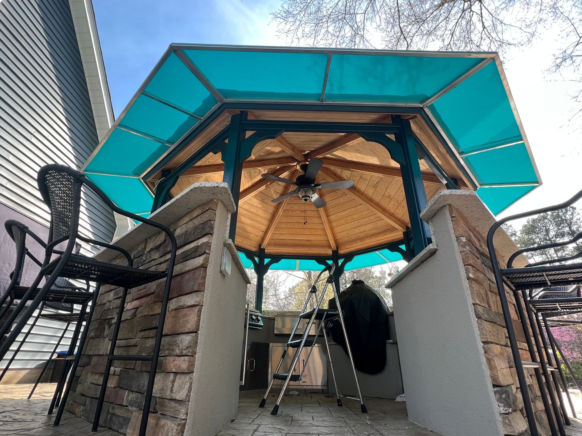 Backyard gazebo with turquoise canopy, wooden roof, ceiling fan, and surrounding patio chairs