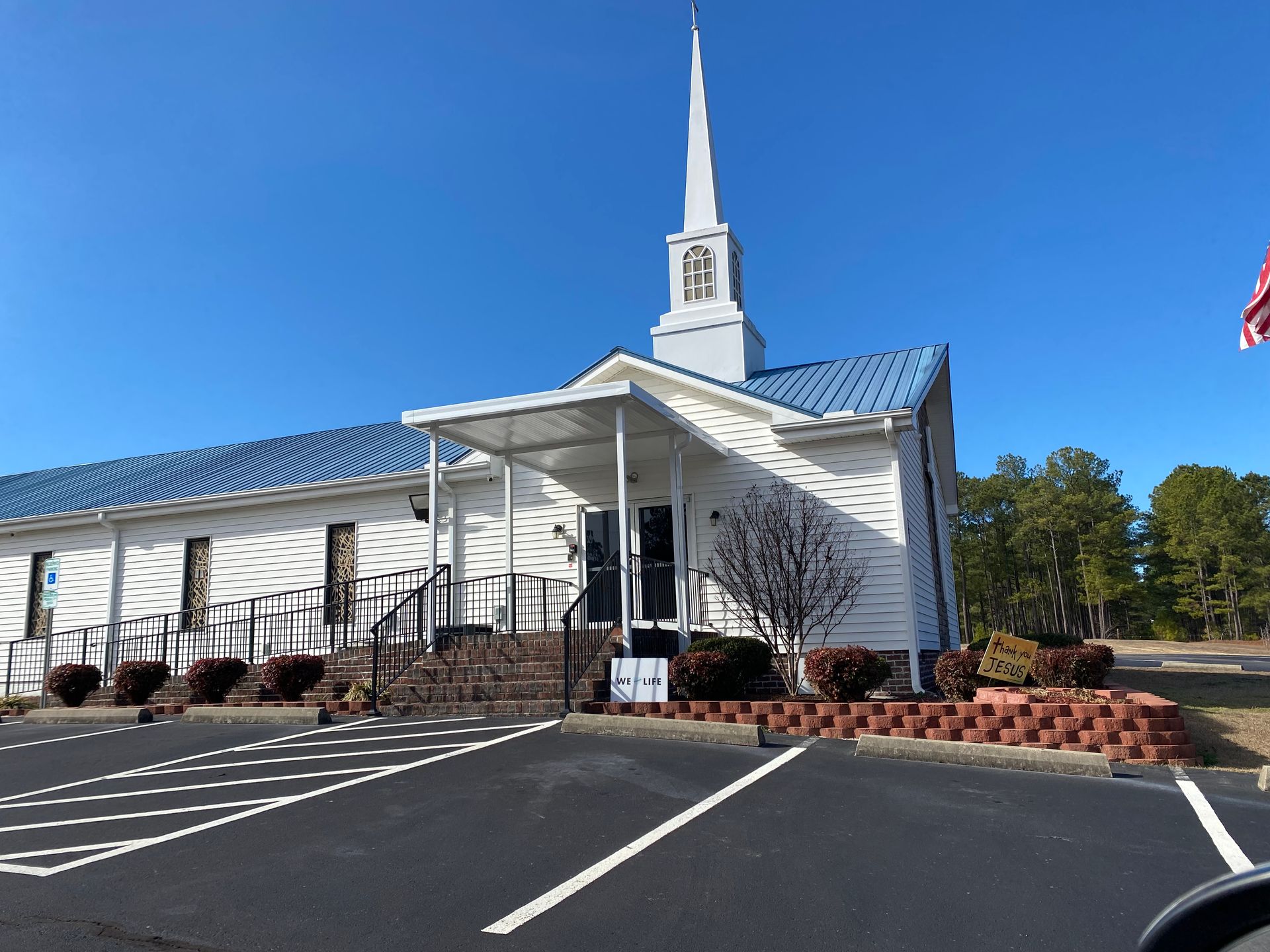White church with tall steeple beside an empty parking lot under a clear blue sky