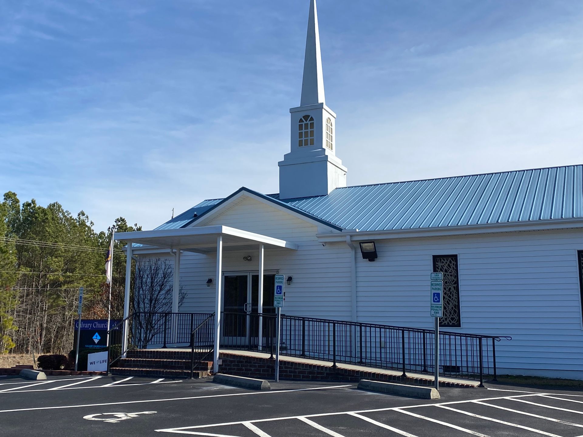 White church with blue roof and steeple, front ramp entrance, under a clear sky