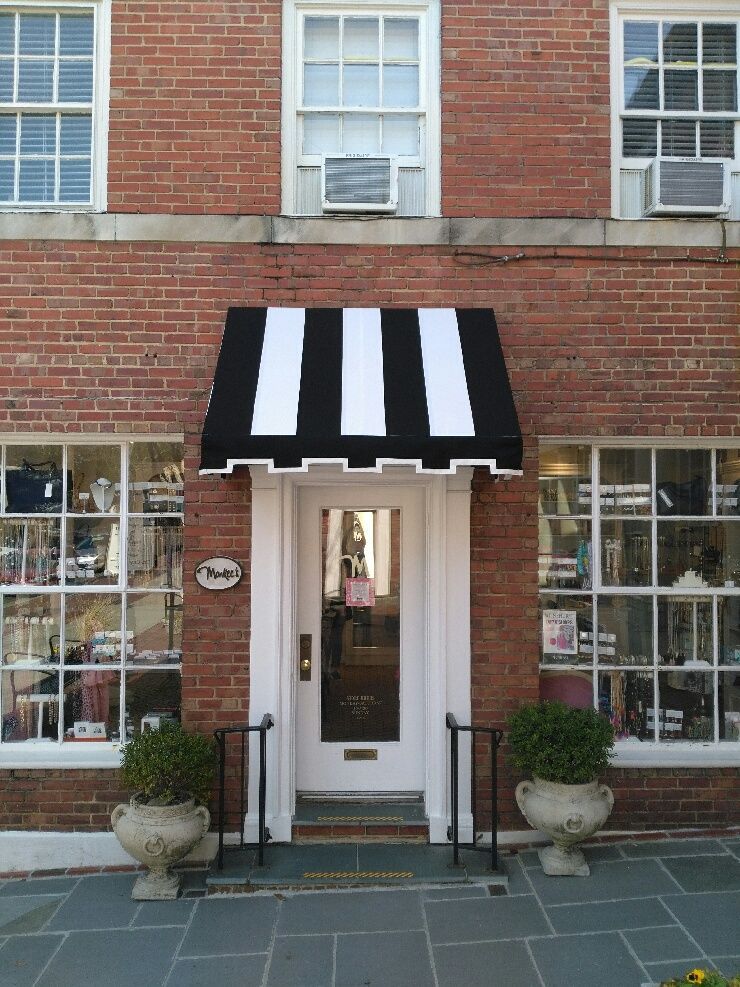 Brick storefront with black-and-white striped awning and white door, flanked by windows and potted plants