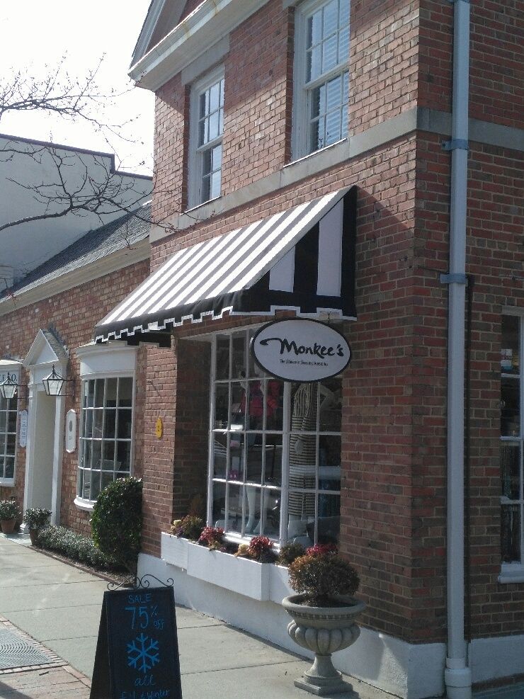Brick storefront with a black-and-white striped awning and round hanging sign on a sidewalk in daylight