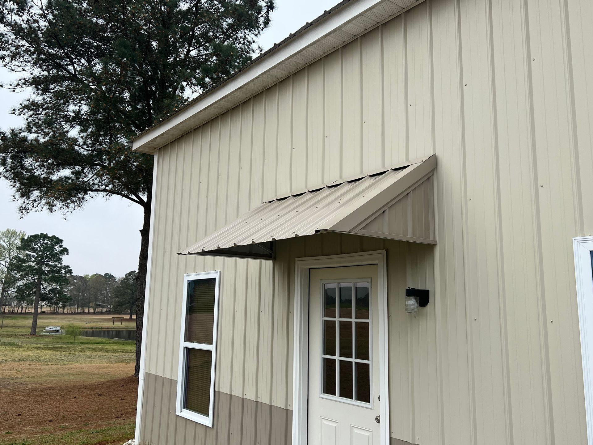Beige building exterior with a white door, window, awning, and wall light