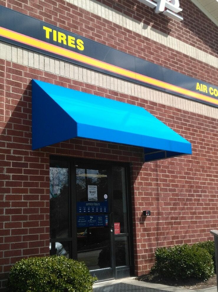 Brick storefront entrance with bright blue awning and yellow “TIRES” sign above the door