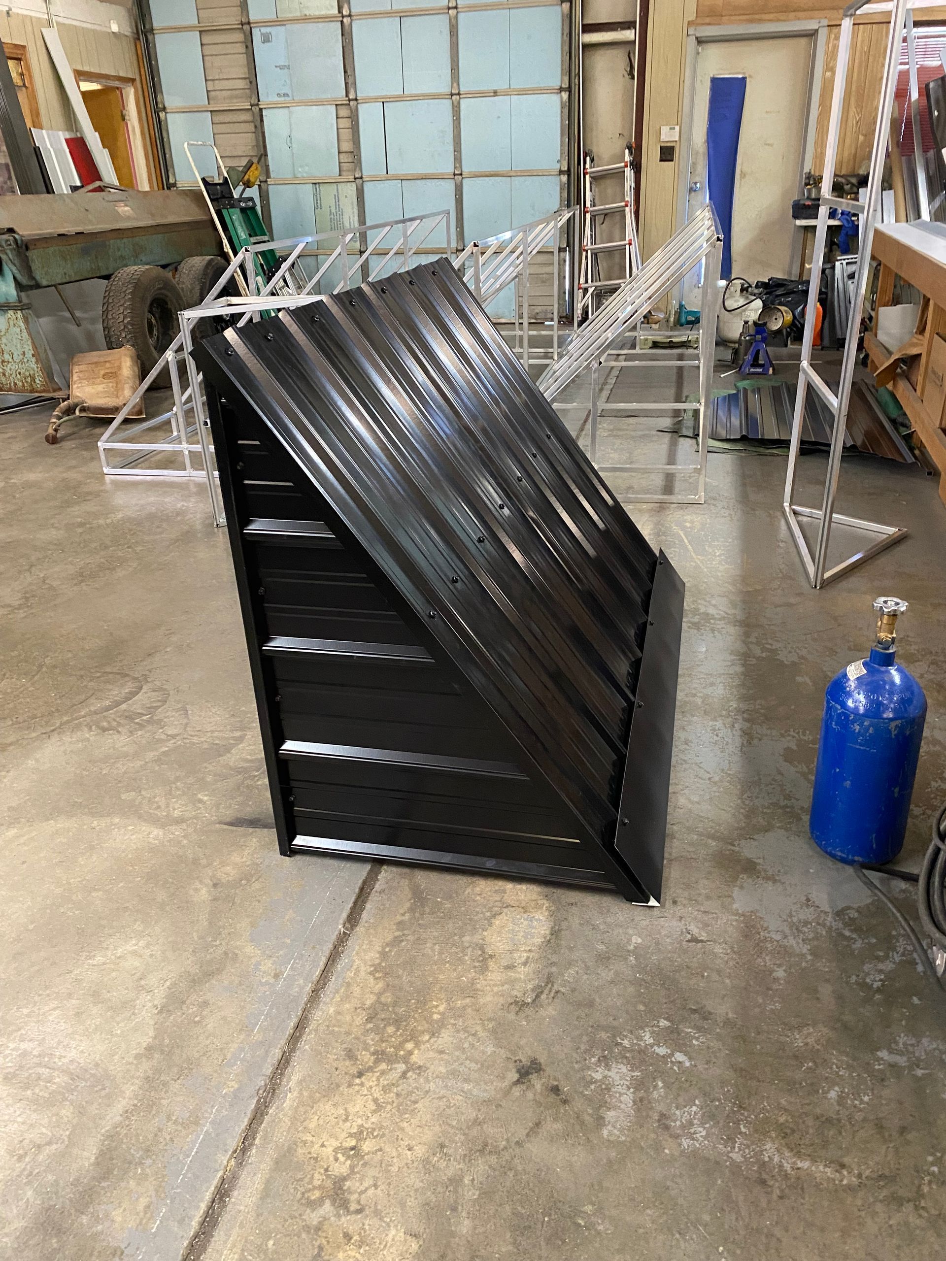 Black metal ramp or enclosure in a workshop, with a blue gas cylinder and tools in the background.