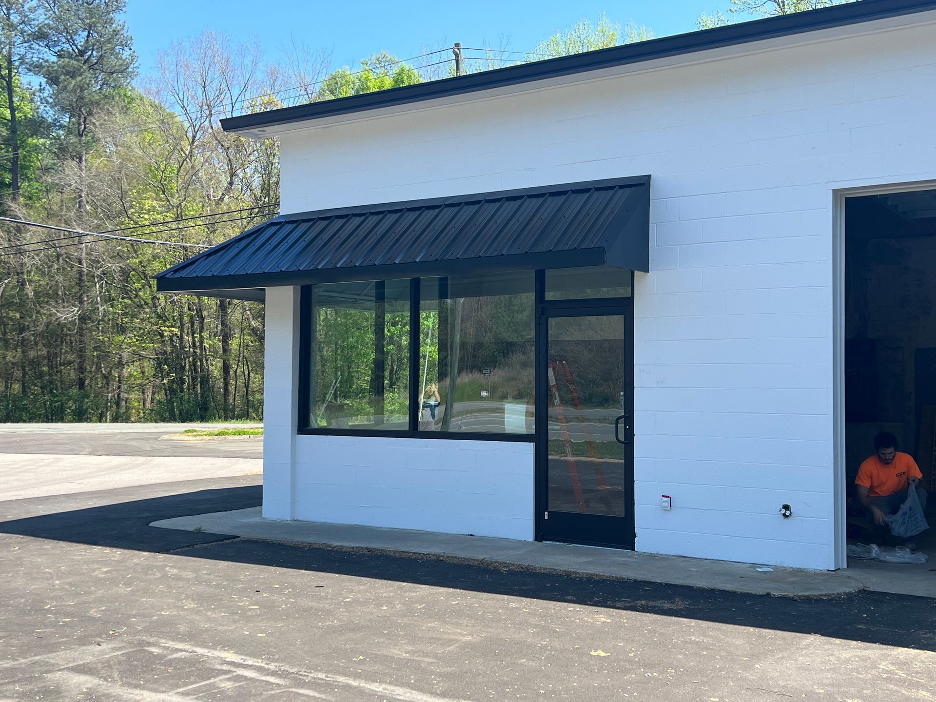 White building with black awning and windows, beside an open garage door with a person sitting inside.