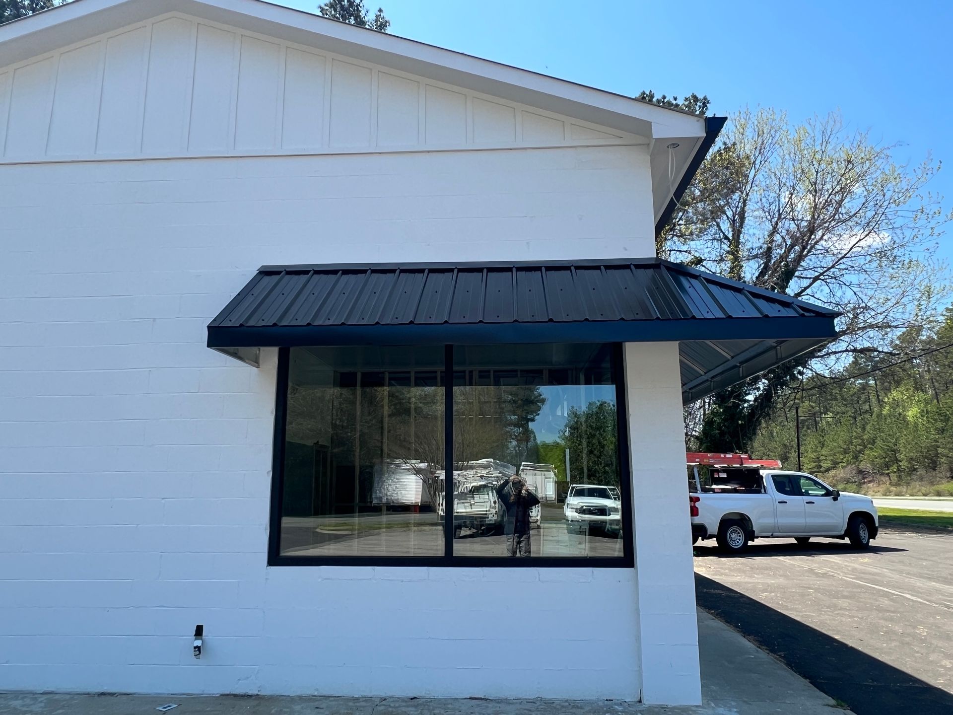 White building exterior with a black awning, large window, and parked white pickup truck outside