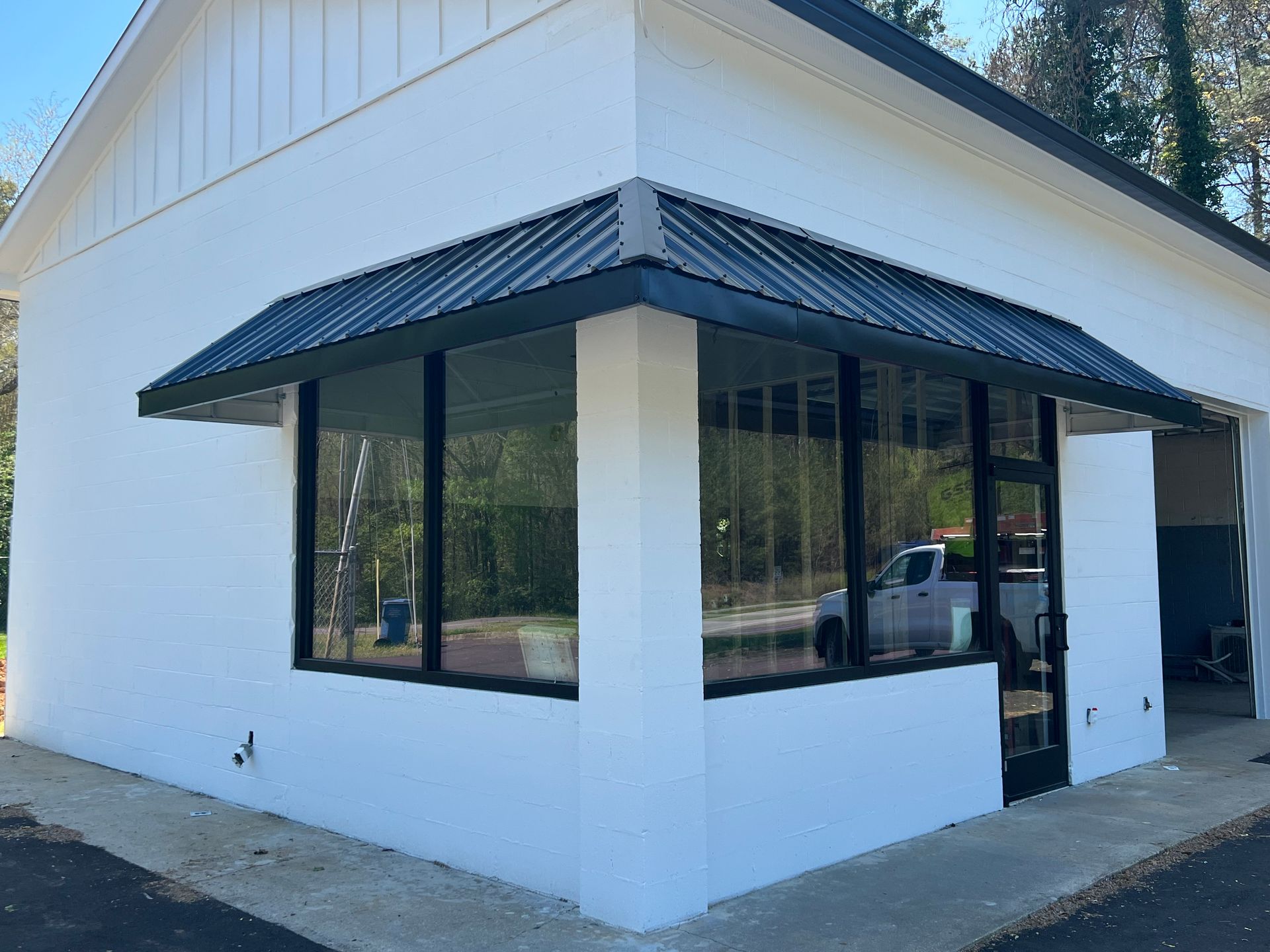 Corner of a white building with black awnings and large windows on a sidewalk