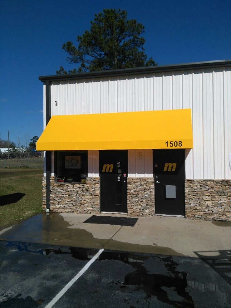 Small building entrance with yellow awning and black doors, with a puddle on the pavement.