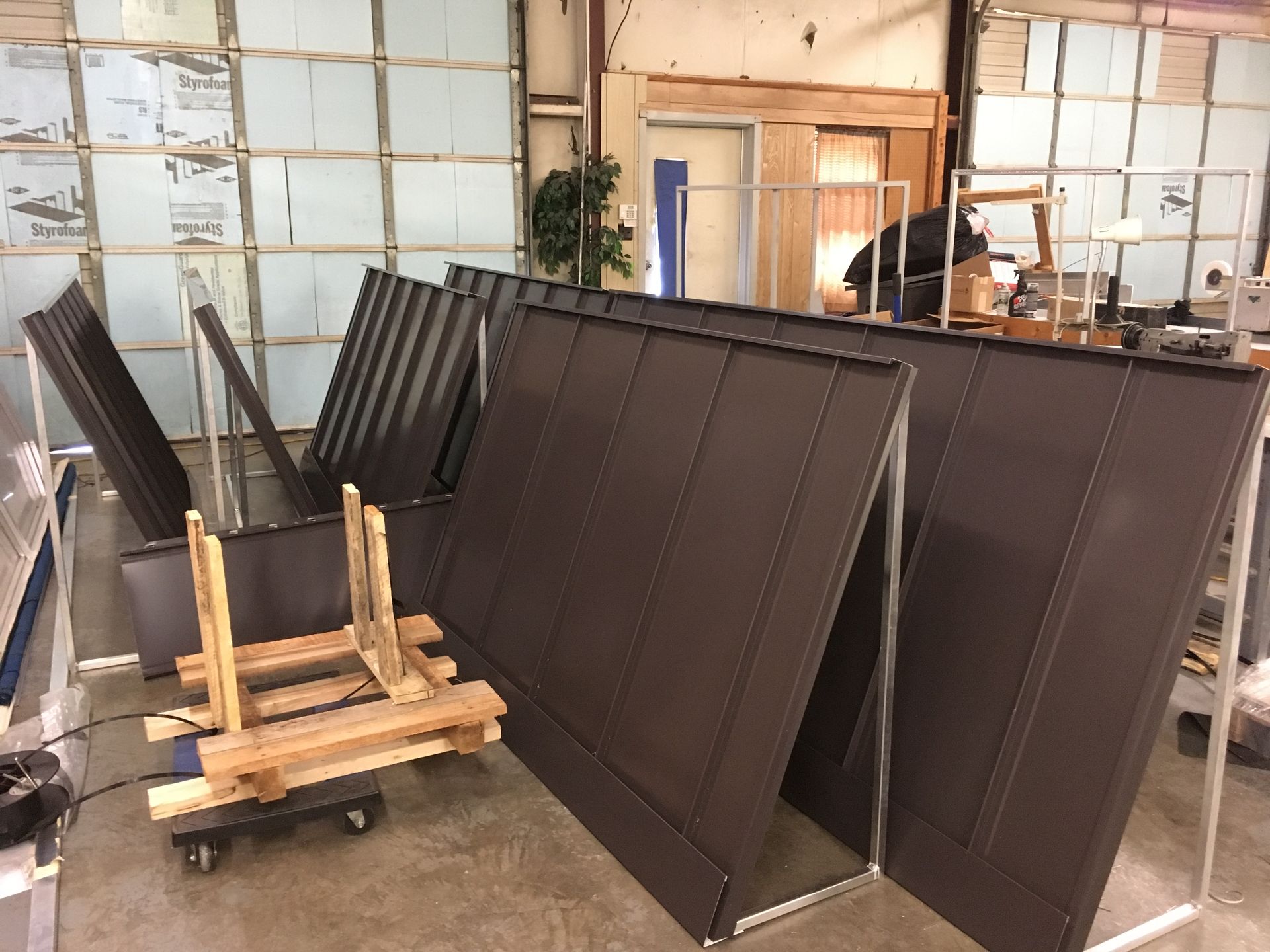 Stacked dark brown panels on dollies inside a warehouse-like room.