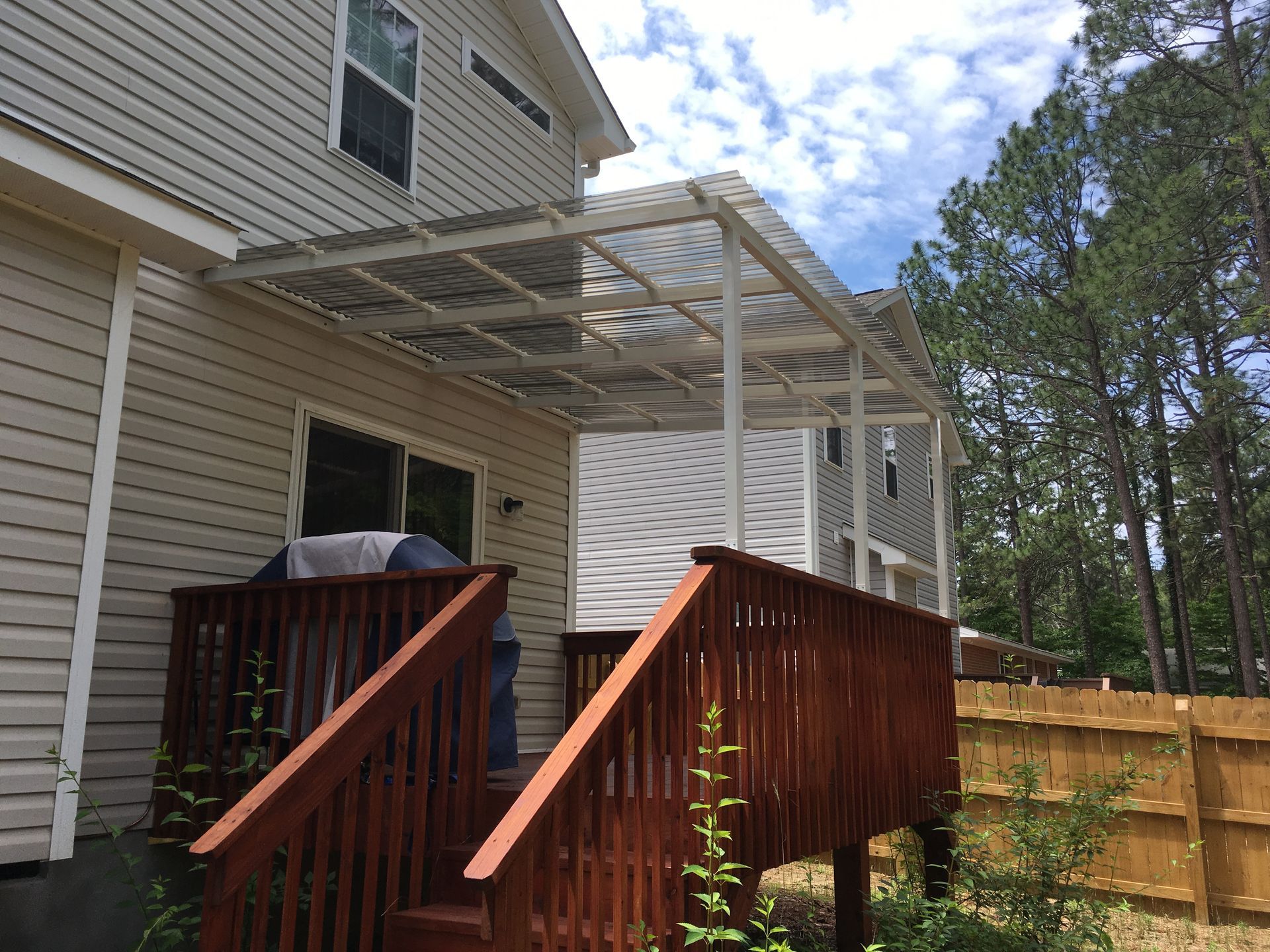 Back deck with wooden stairs and railing beside a beige house, under a partially built roof frame