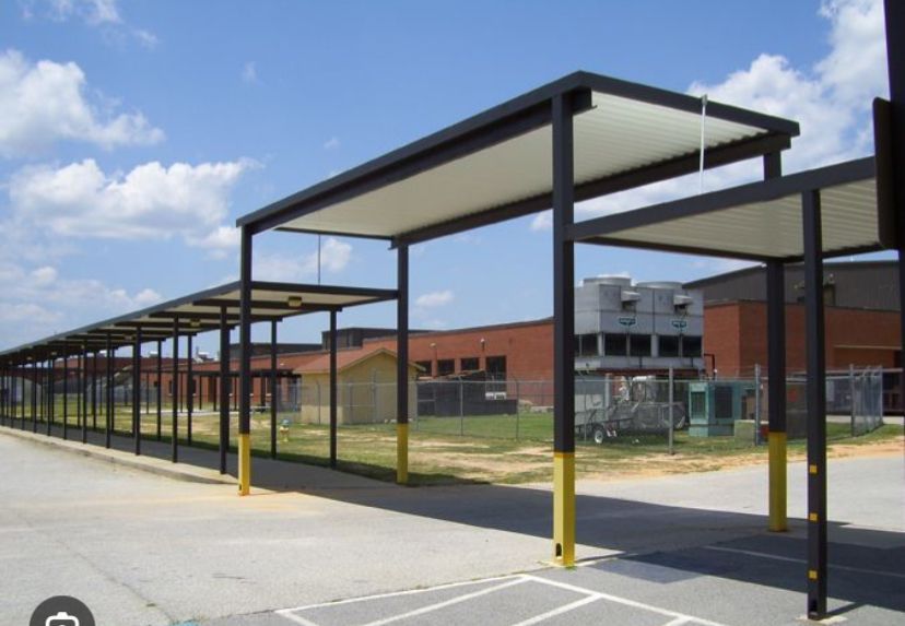 Covered walkway with yellow posts leading to a brick school building under a partly cloudy sky