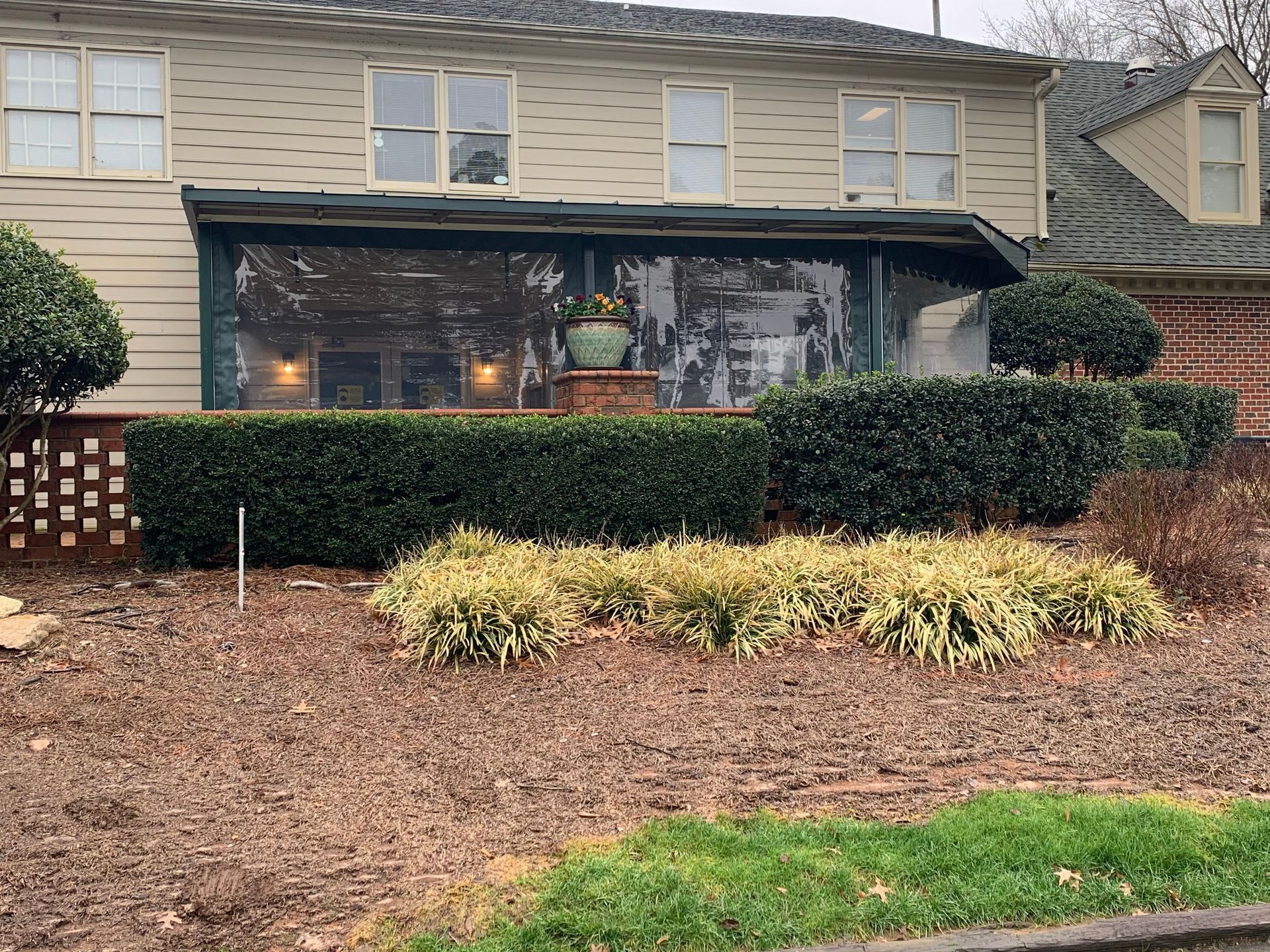 Suburban townhouse exterior with a screened porch, trimmed hedges, and a mulch-covered front bed