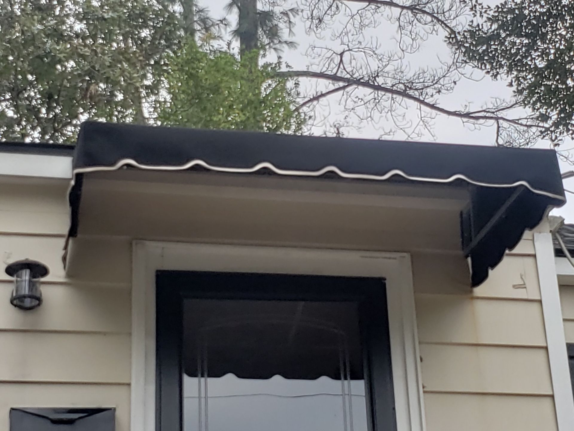 Black awning over a white house entrance with a glass storm door and wall light