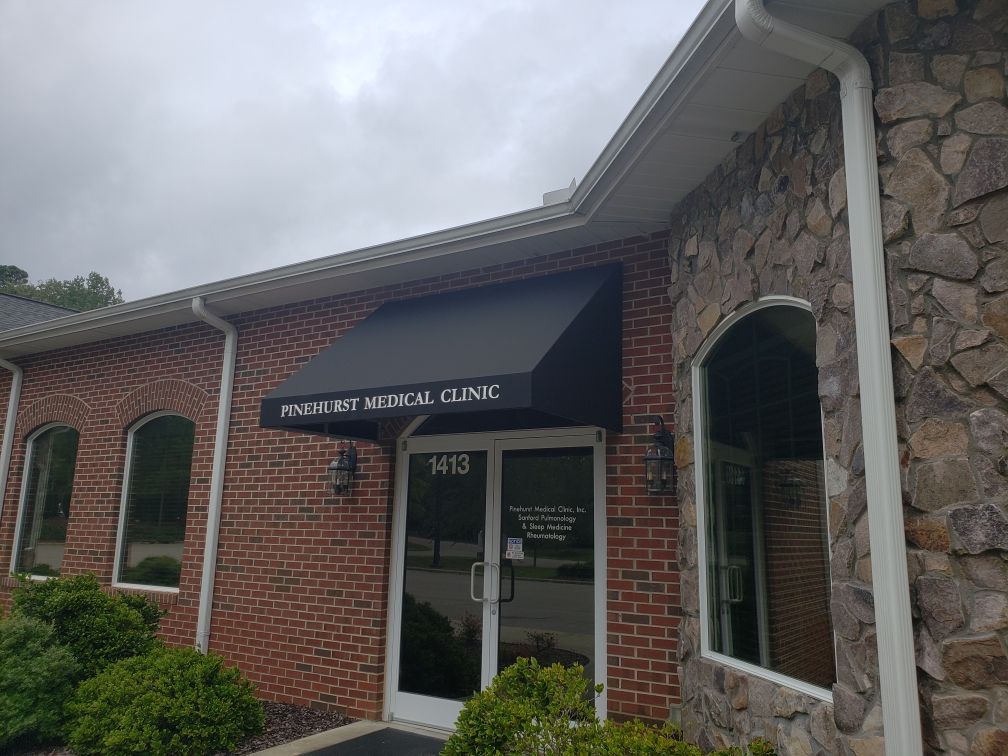 Brick medical clinic entrance with black awning and glass doors under a cloudy sky