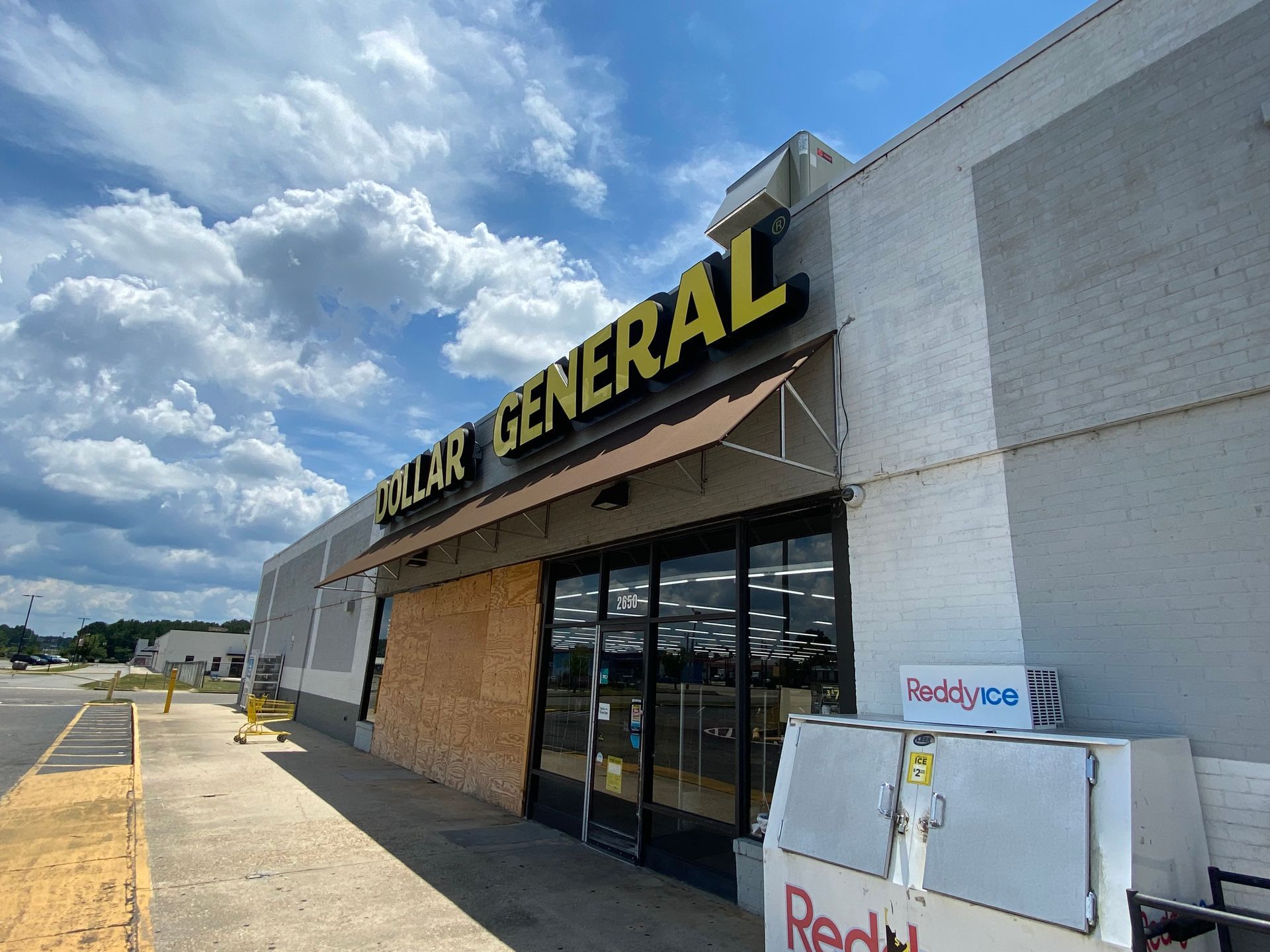 Dollar General storefront in a strip mall under a cloudy sky, with a sidewalk and parking lot.