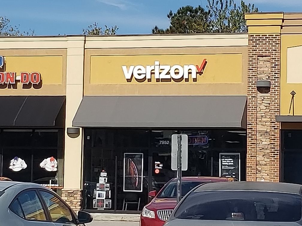 Verizon storefront with gray awning and parked cars in front