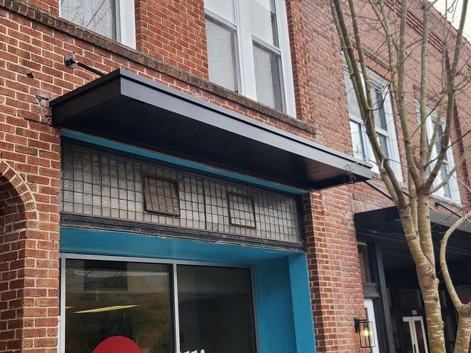 Brick building entrance with black awning, blue trim, and a leafless tree beside the doorway