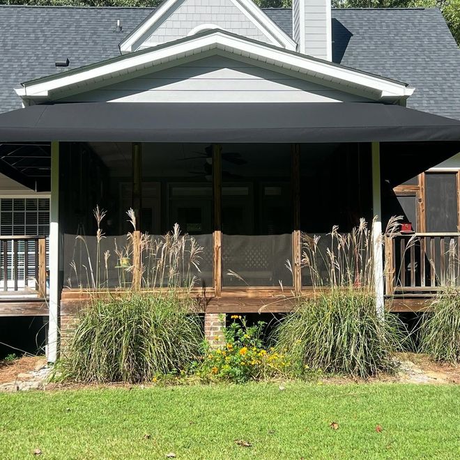 Front porch with black awning, porch railings, and tall ornamental grasses in front of a house