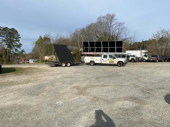 Gravel lot with trucks, a white trailer, and a large black ramp under a clear sky