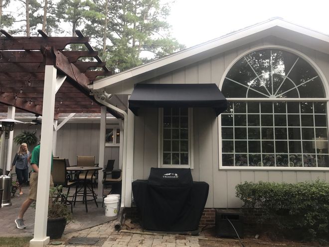 Backyard patio with pergola, black grill, and large arched window on a white house