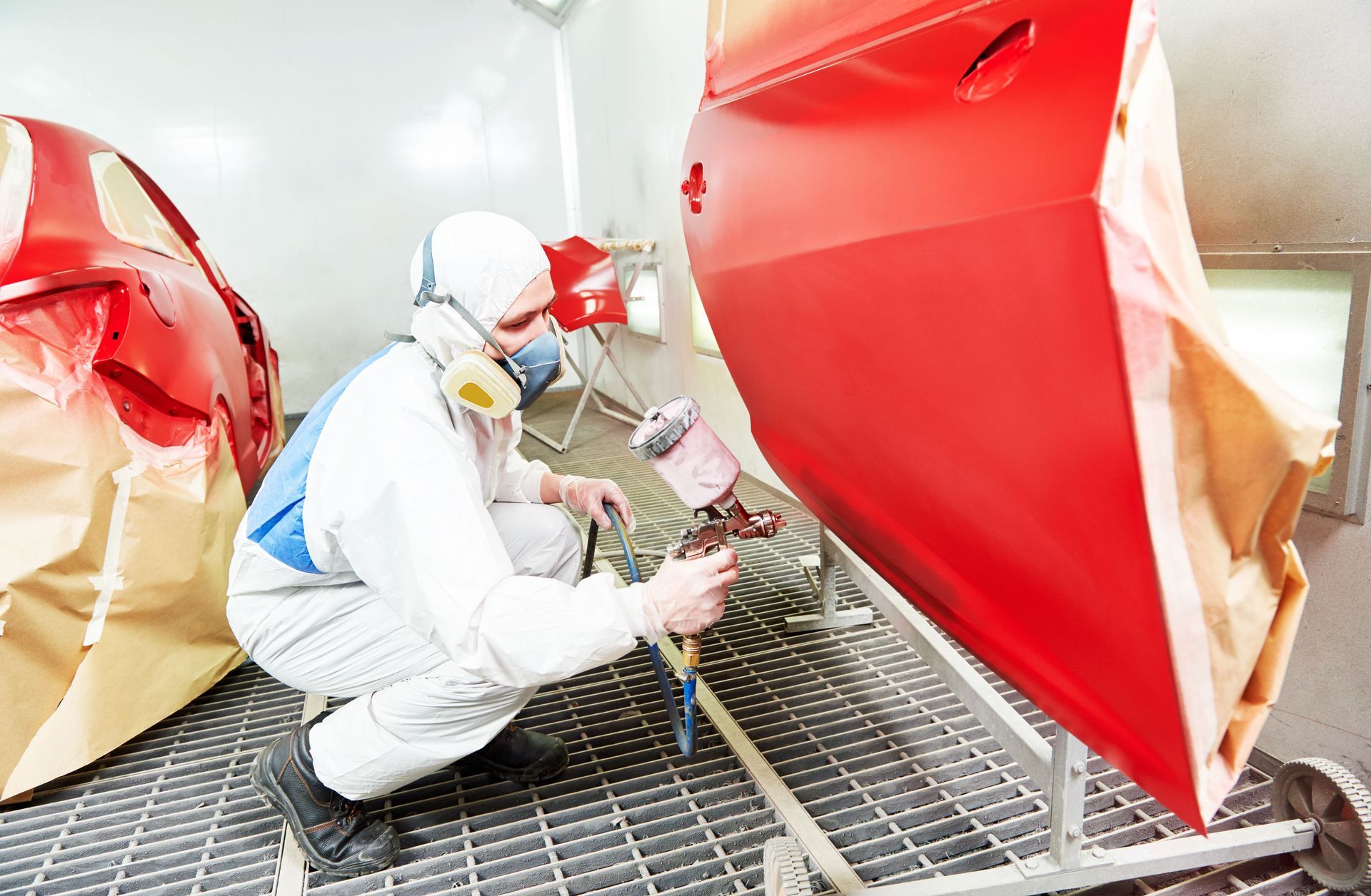 Worker in white protective suit spray-paints a red car body in an auto shop