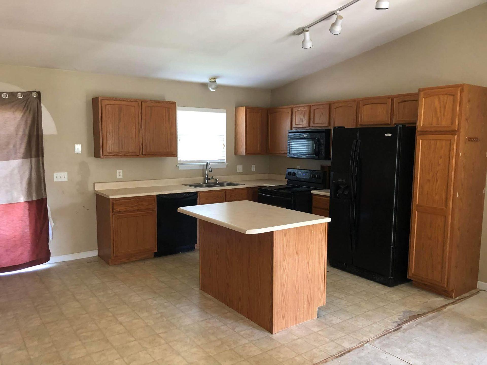 A kitchen with oak cabinets, black appliances, a central island, and beige tile flooring under a sloped ceiling.