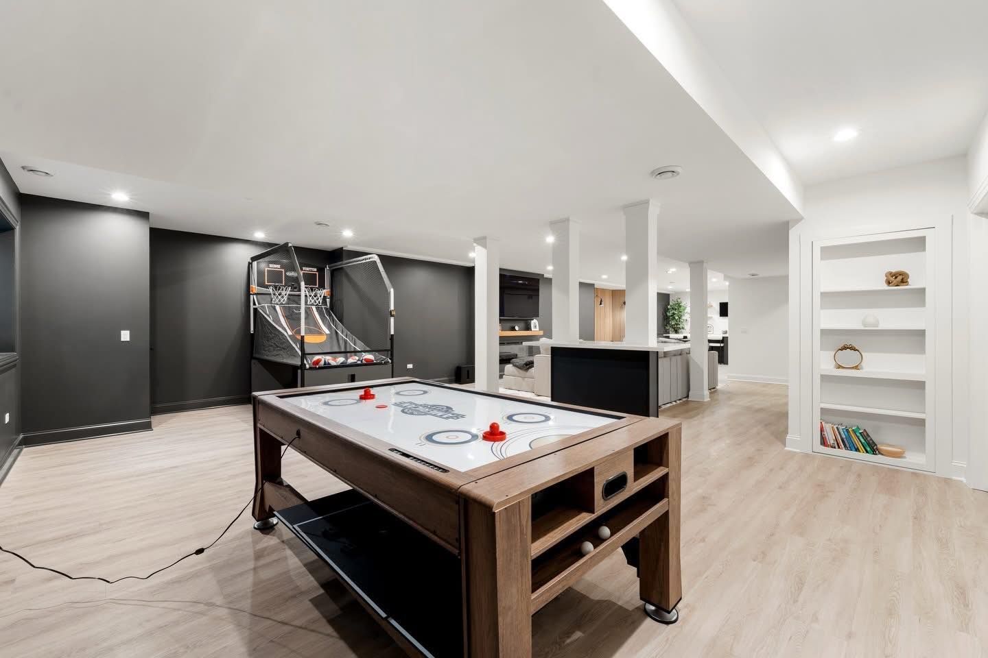 Game room with air hockey table, basketball game, and built-in shelves; neutral tones.