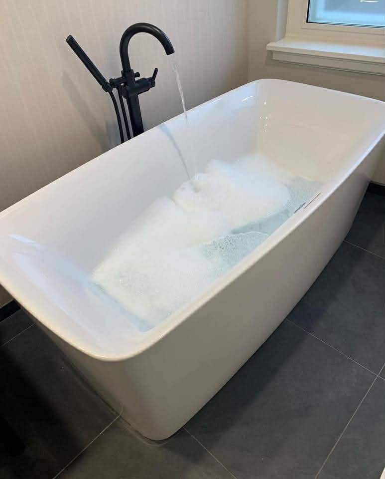 White bathtub filling with water, black faucet, and gray tile floor.