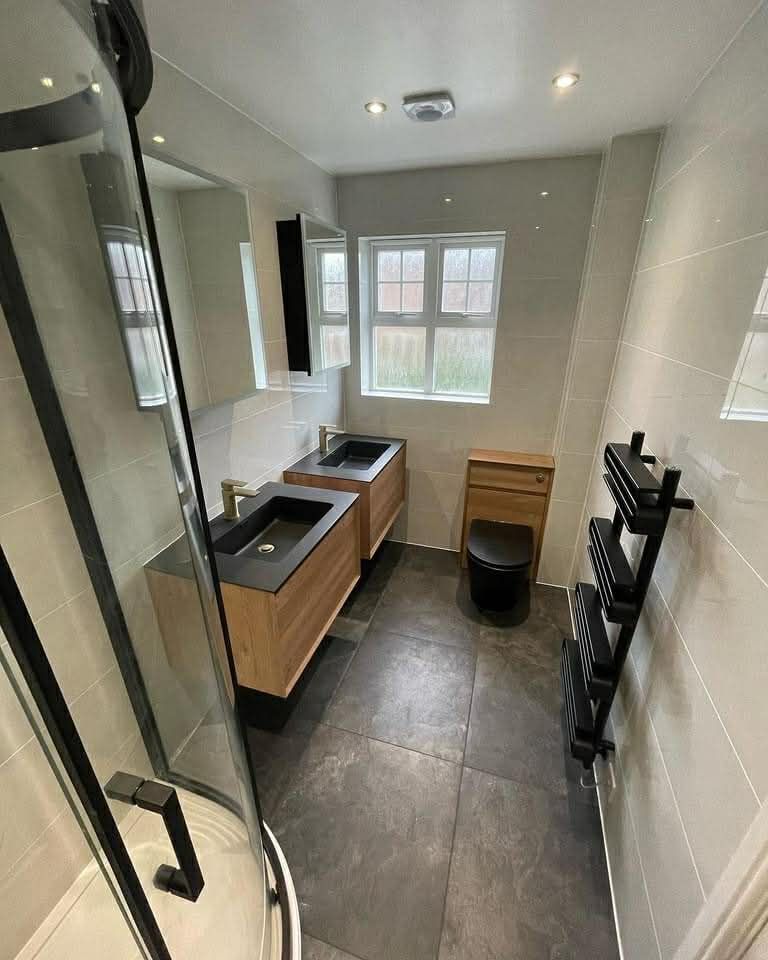 Modern bathroom with double sink vanity, toilet, and shower. Dark tile floor, light walls.