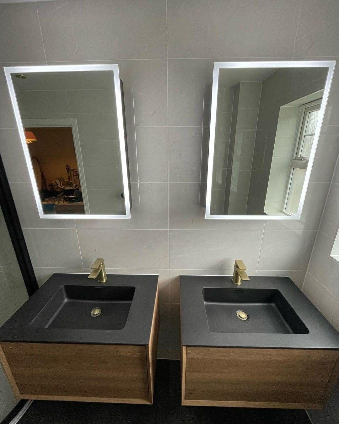 Two bathroom vanities with black sinks, gold faucets, and lighted mirrors.
