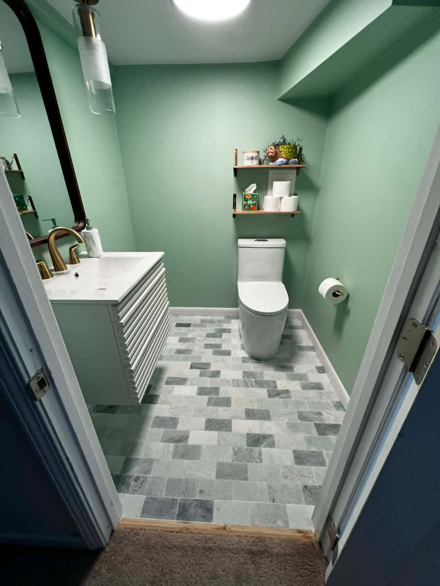 Small bathroom with green walls, patterned floor, white toilet, and sink.