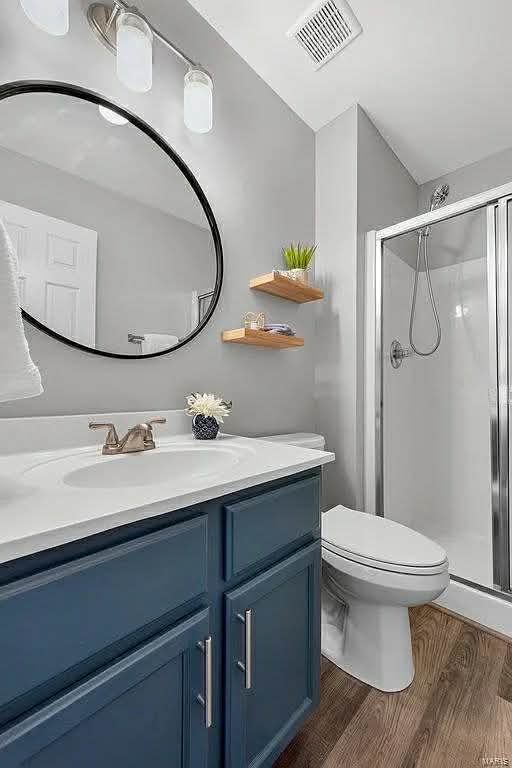 Modern bathroom with a blue vanity, white countertop, round black mirror, two floating wood shelves, and a walk-in shower.