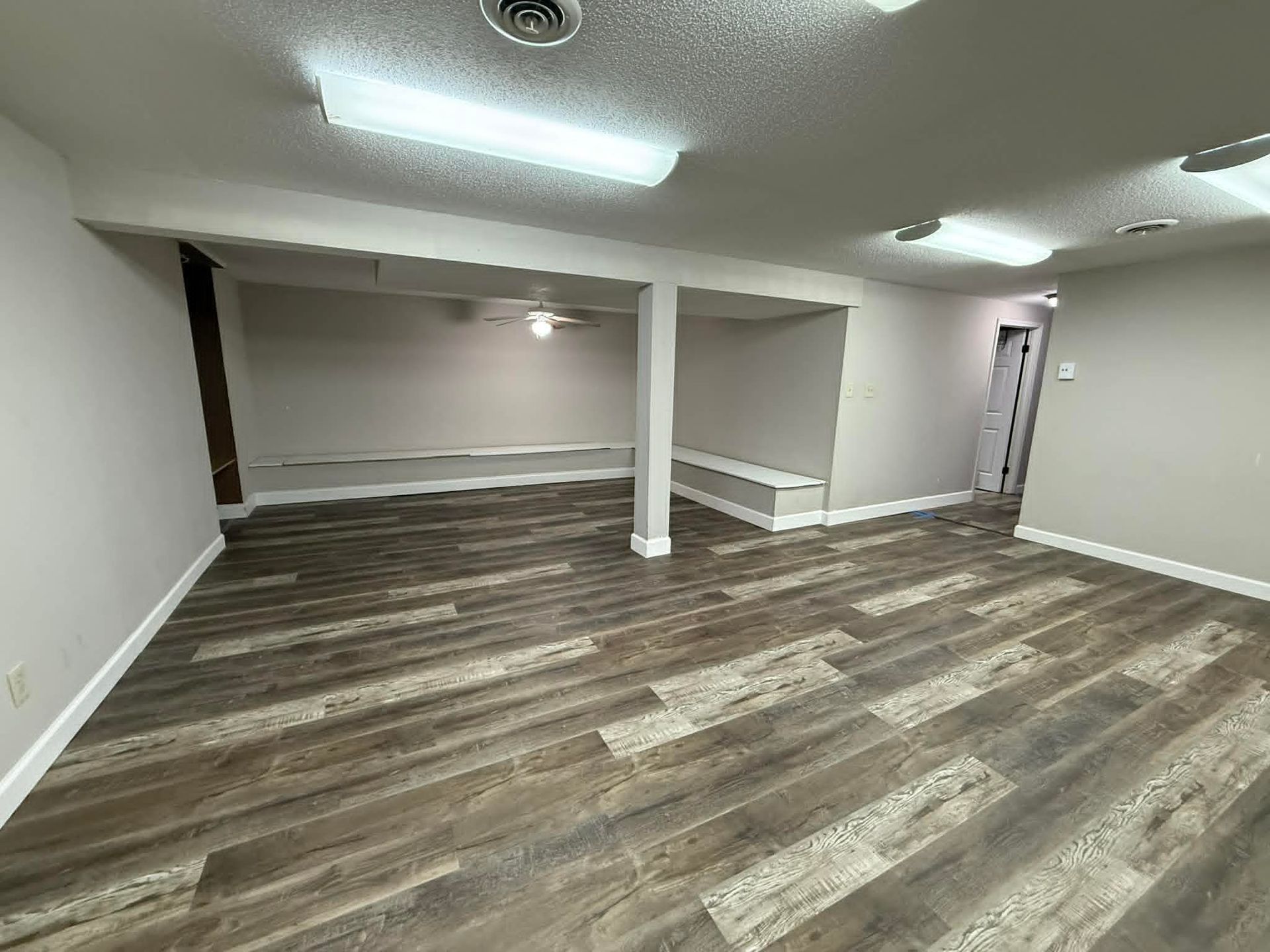 Spacious room with wood-look flooring, white walls, support columns, and recessed lighting.