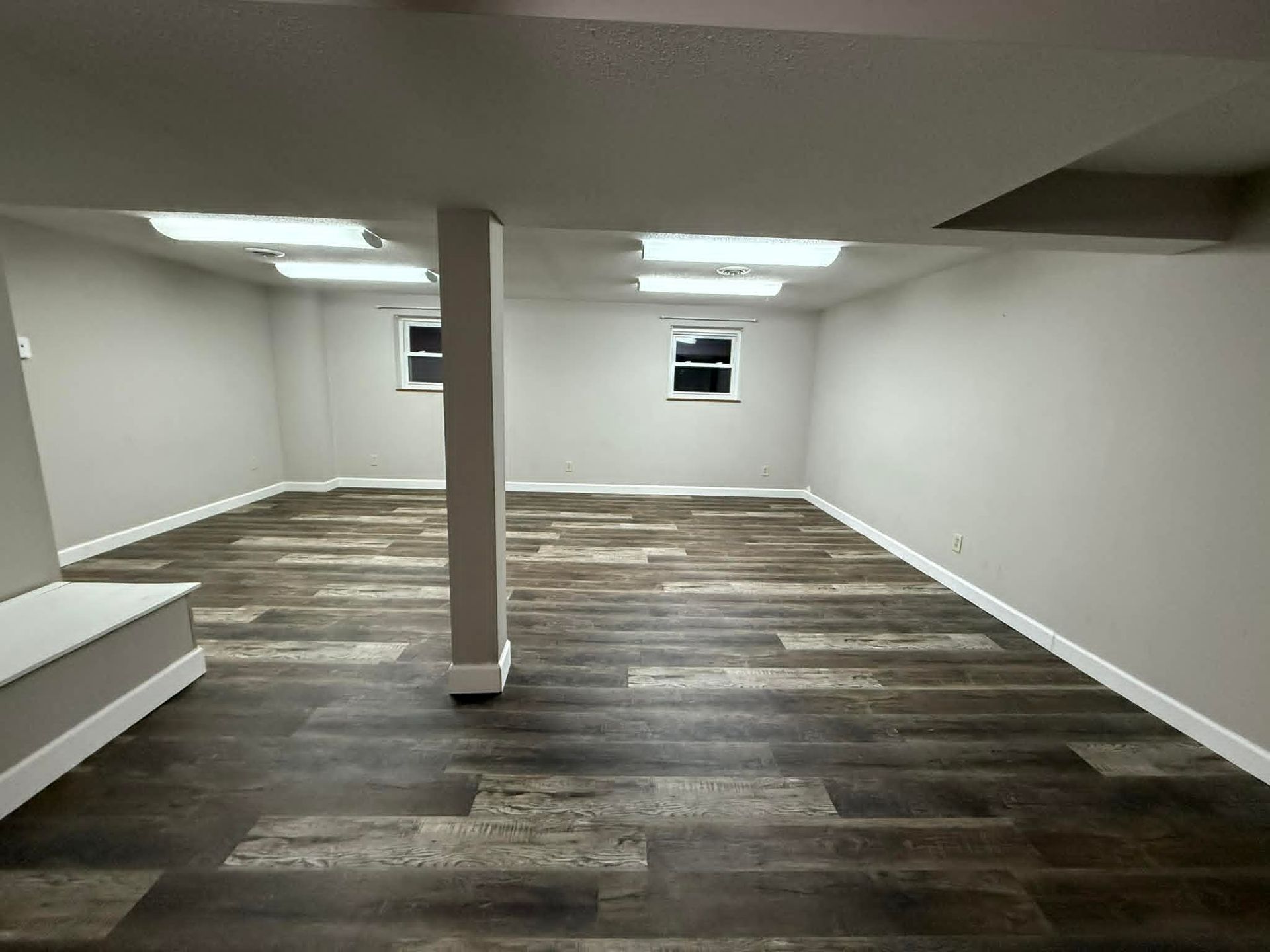 Empty, recently renovated basement room with gray walls, dark wood-look flooring, and recessed lighting.