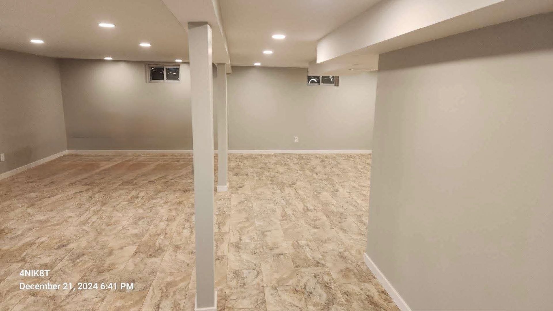 Empty basement with beige flooring, gray walls, support columns, and recessed lighting.