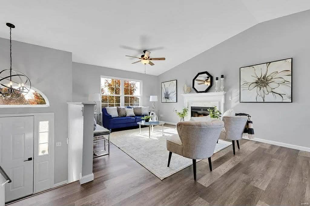 A bright, modern living room with light gray walls, wood-look flooring, a blue sofa, two beige chairs, and a fireplace.