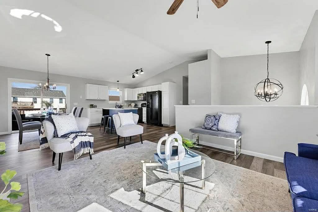 An open-concept living area with white furniture, a shaggy rug, a dining space, and a kitchen with black appliances.