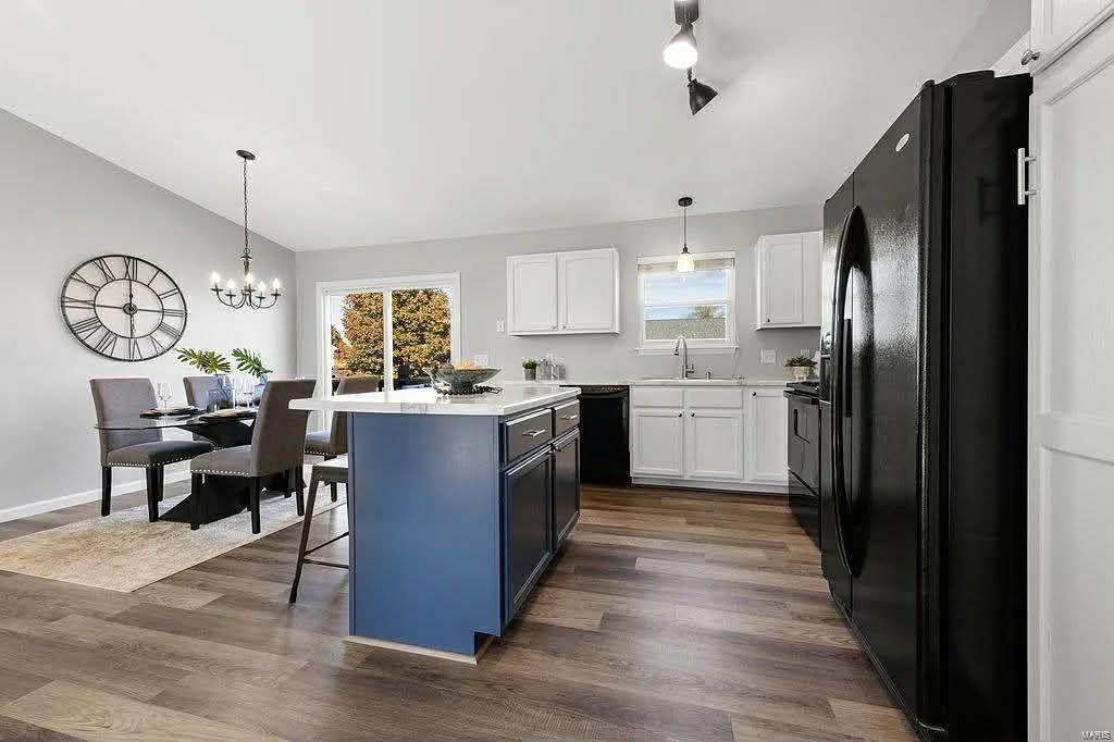 Modern kitchen and dining area with a blue island, white cabinets, black appliances, and a table for four.