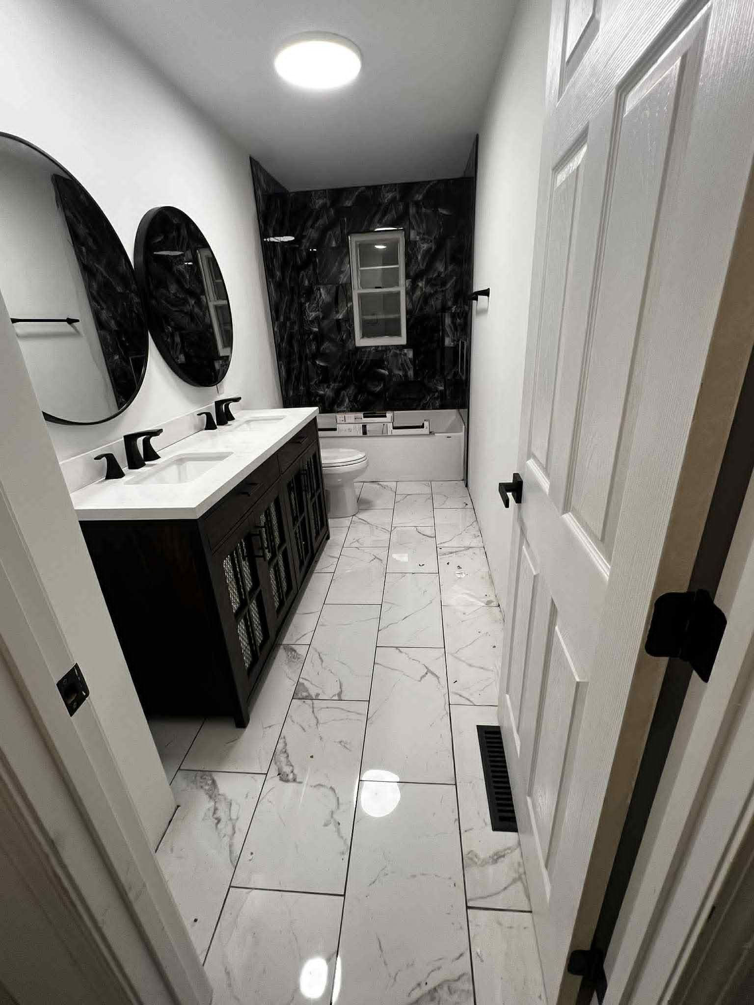 A newly renovated bathroom with black and white accents. Features include a vanity with two sinks, and a tiled floor.