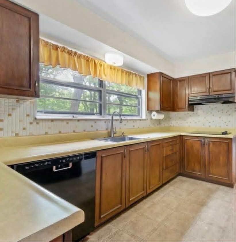 Modern white kitchen with stainless steel appliances, gold hardware, and a window overlooking greenery.