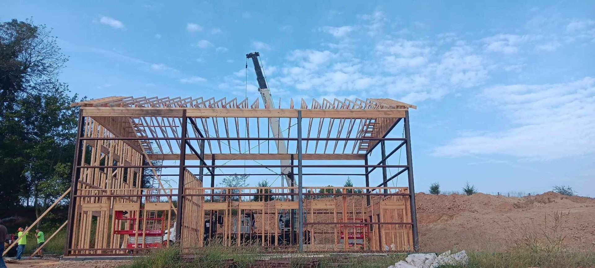 Construction of a metal and wood framed building under a blue sky. Crane visible.