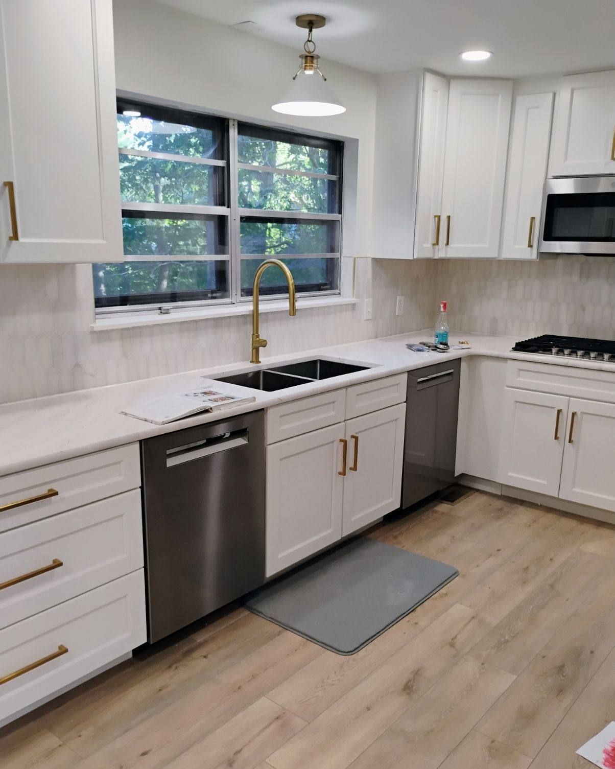 White kitchen with stainless steel appliances, gold fixtures, and light wood floors.