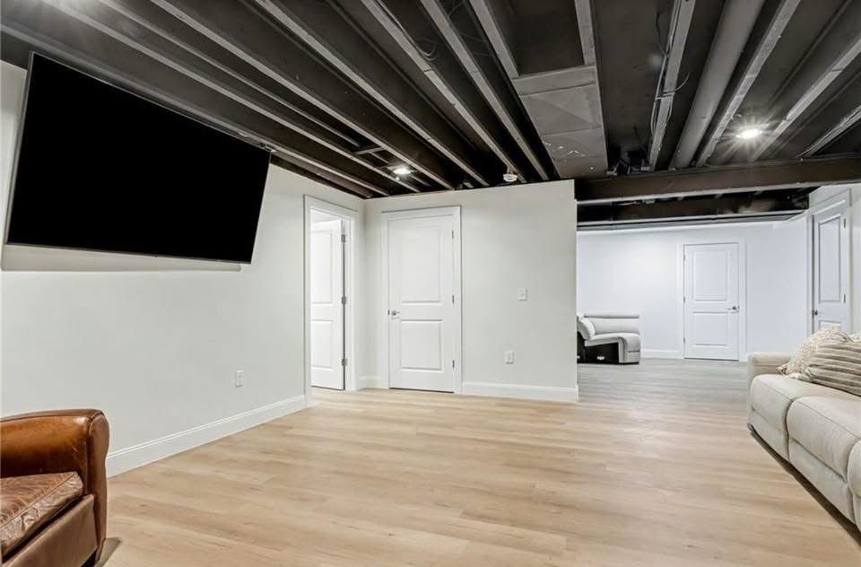 Finished basement with black ceiling, white walls, wood floor, TV, and seating.