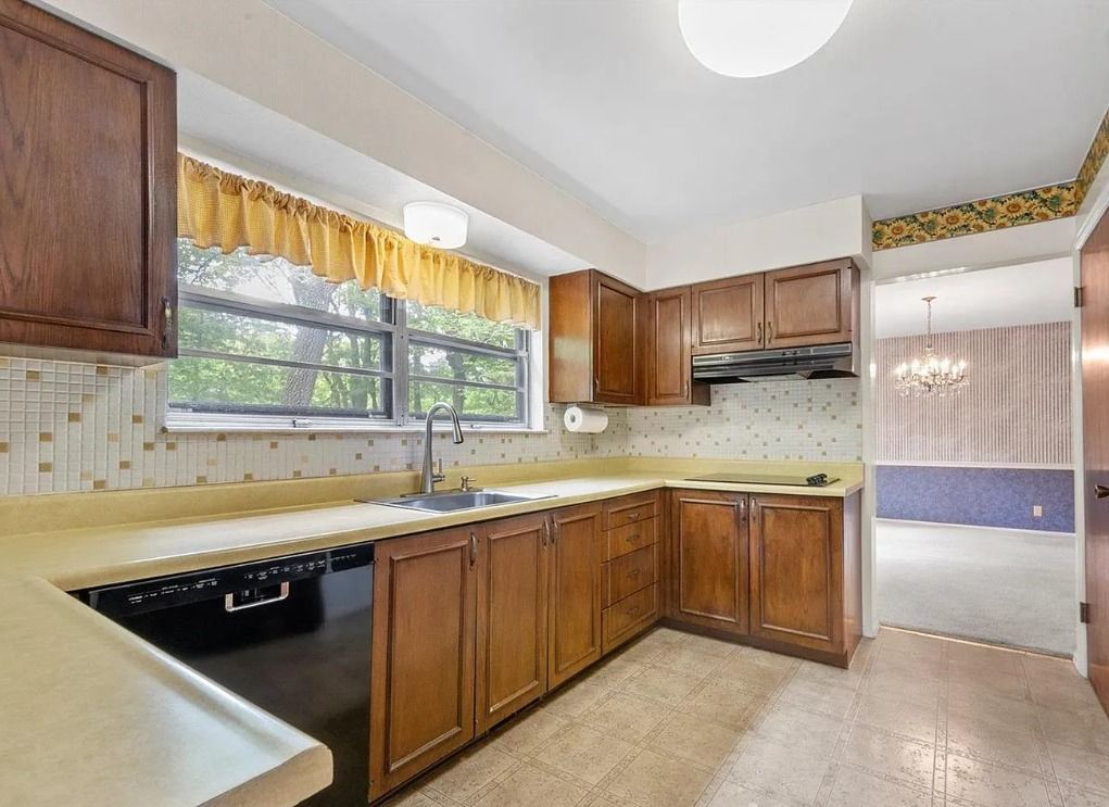 Kitchen with wooden cabinets, beige countertops, and a window overlooking greenery.